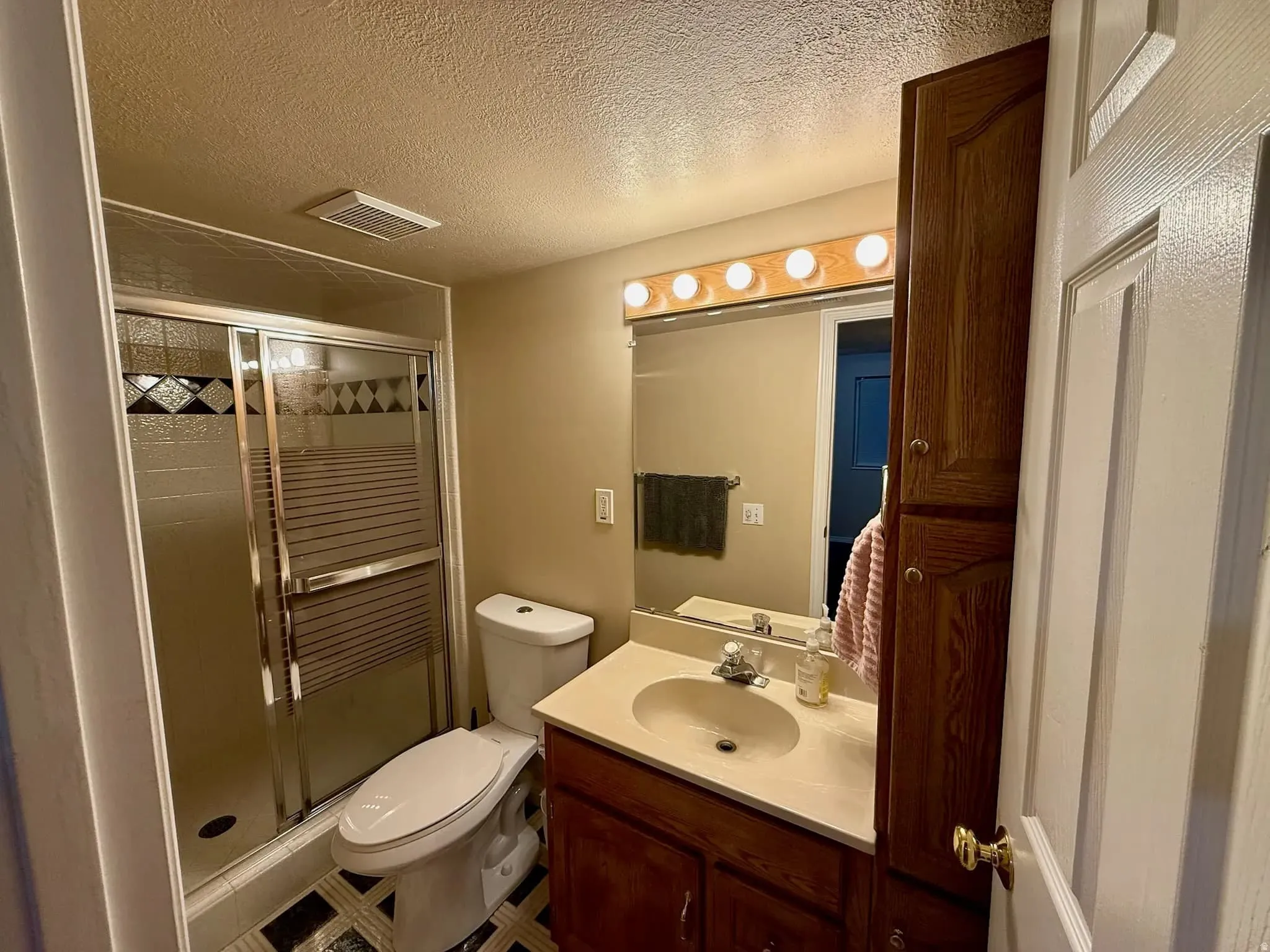 Bathroom featuring a glass-enclosed shower with decorative accent tiles, a single vanity with an integrated sink and light-toned countertop, a large wall mirror, and a built-in wood-finish cabinet