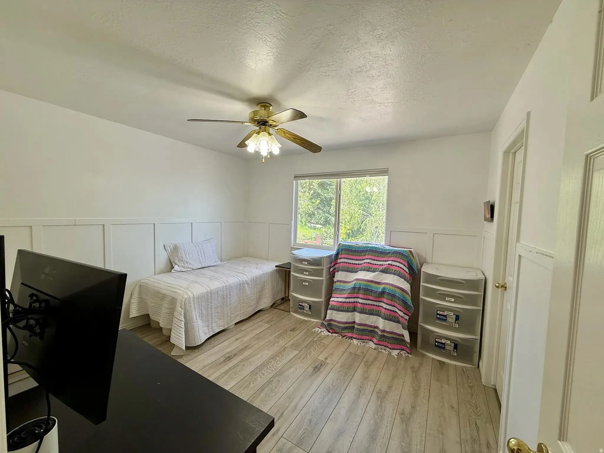 Room featuring wood-finish flooring, white paneling, and a single window offering natural illumination