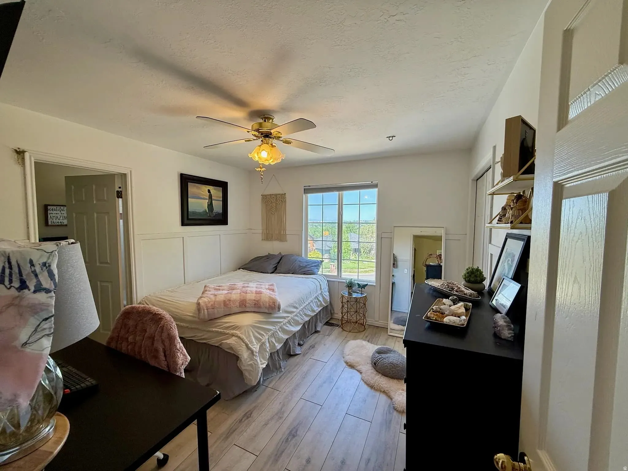 Bright bedroom featuring wood-finish flooring, a window offering exterior views, and a ceiling fan with integrated lighting