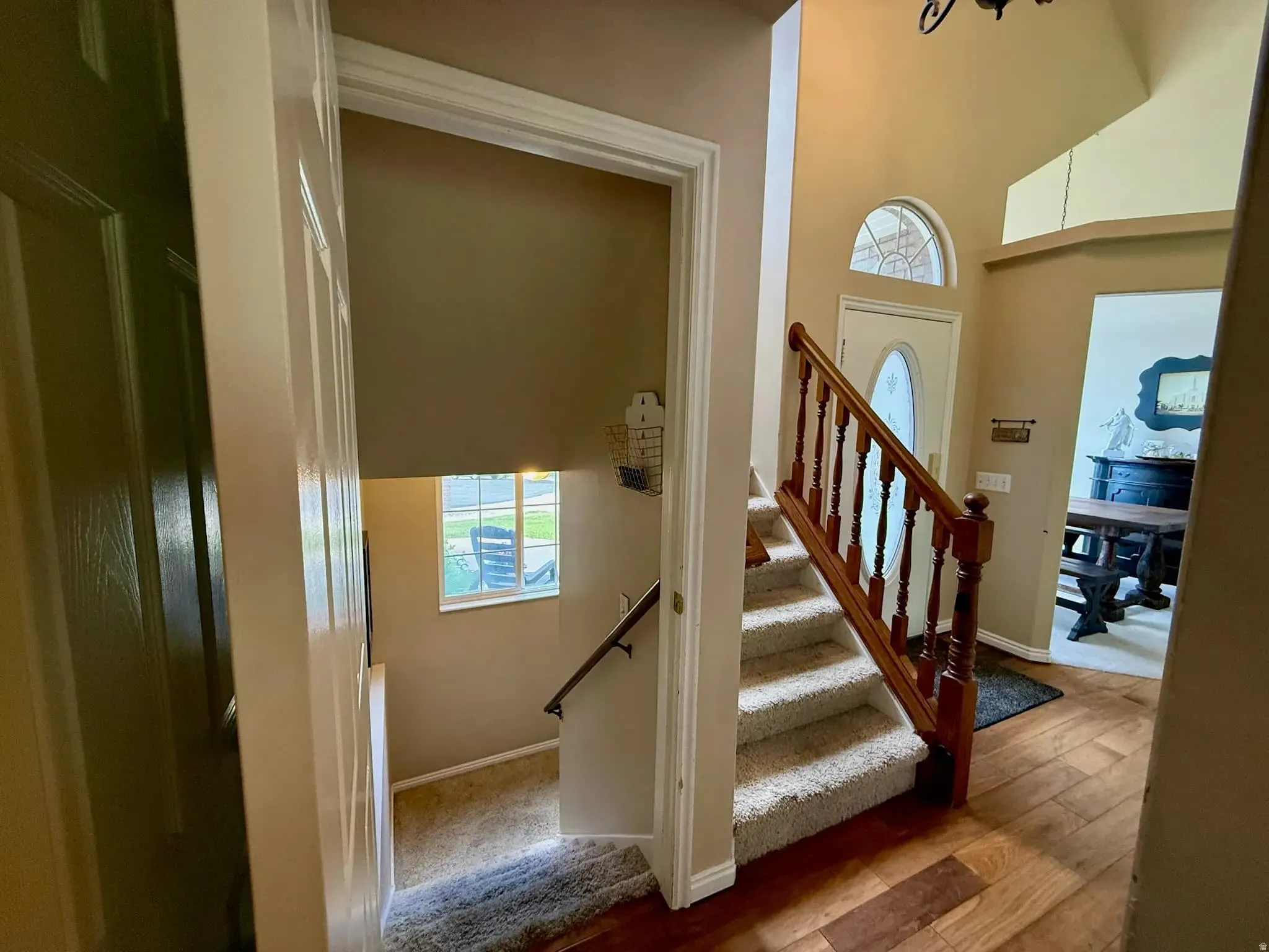 Entryway featuring wood-finish flooring, a white paneled door with an oval glass insert, an arched transom window, and a carpeted staircase with a wood handrail and balusters