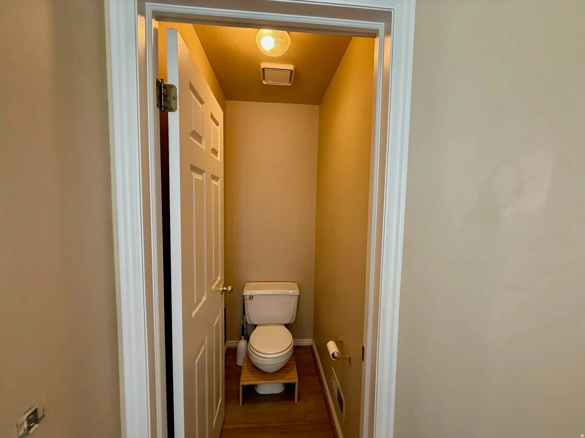 Powder room featuring a standard white toilet and wood-finish flooring