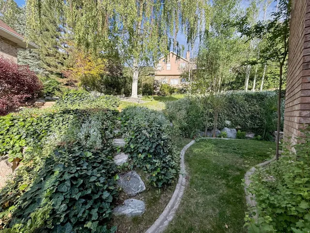 Expansive terraced yard featuring natural rock steps, manicured lawn, established shrubbery, mature trees, and a brick exterior element