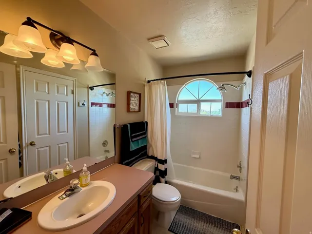 Full bathroom featuring a white porcelain vanity sink, wood-finish cabinetry, a tub/shower combination, and a decorative arched window