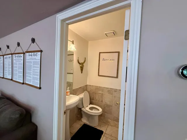Powder room featuring a pedestal sink, toilet, and tiled walls and flooring