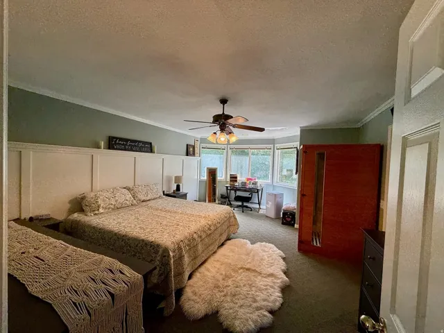Spacious bedroom featuring a bay window, crown molding, a built-in paneled headboard, and a ceiling fan with integrated lighting