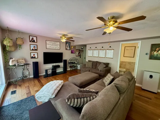 Living area featuring wood-finish flooring, light tan wall paint, and two ceiling fans with integrated lighting