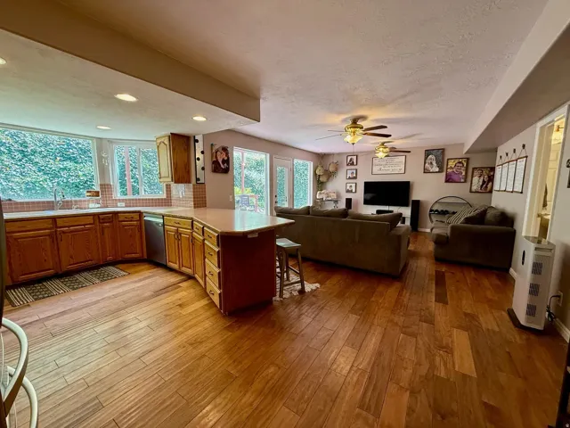 Open-concept living area featuring wood-finish flooring throughout, a kitchen with wood cabinetry and a bay window, and recessed lighting