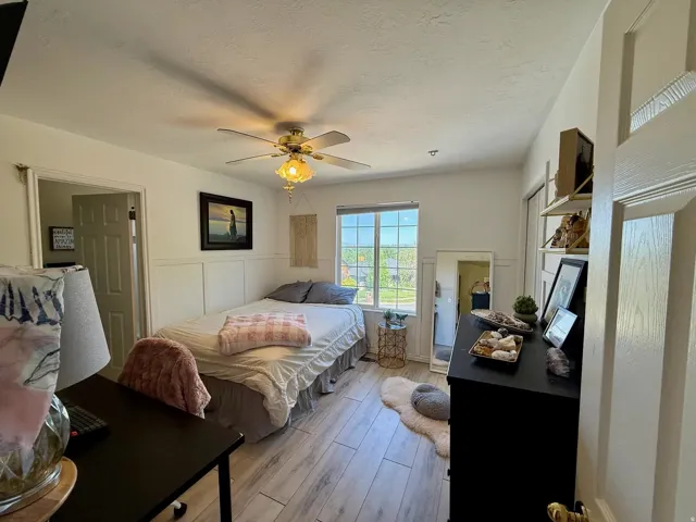 Bright bedroom featuring wood-finish flooring, a window offering exterior views, and a ceiling fan with integrated lighting