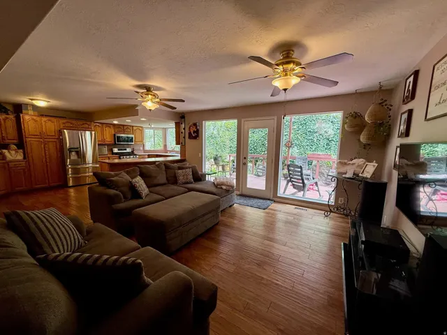 Open-concept living area featuring wood-finish flooring, a full kitchen with stainless steel appliances, multiple ceiling fans, and direct access to an outdoor deck