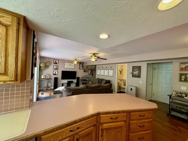 Kitchen with wood cabinetry and a tile backsplash open to a living area with wood-finish flooring, ceiling fans, and recessed lighting