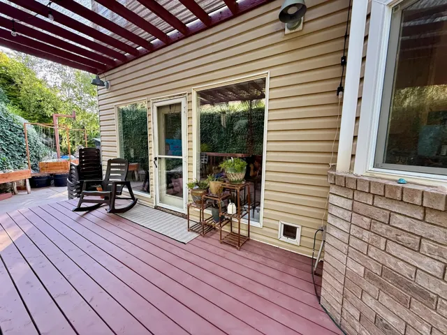Expansive outdoor deck with rich red-toned wood-finish flooring, a pergola structure, and direct access through a glass-paneled door