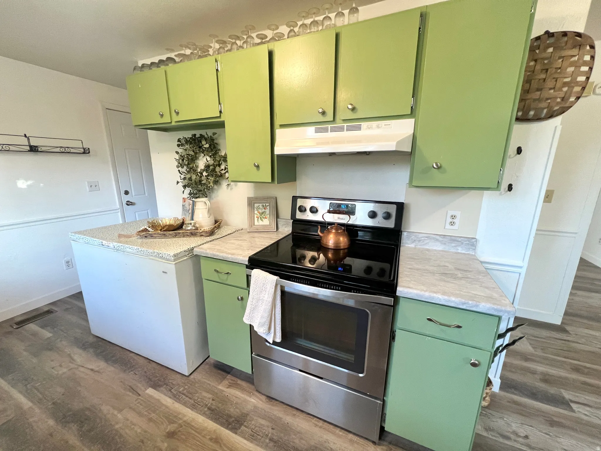 Kitchen featuring wood-finish flooring, light-toned countertops, green cabinetry, and a stainless steel range with overhead ventilation