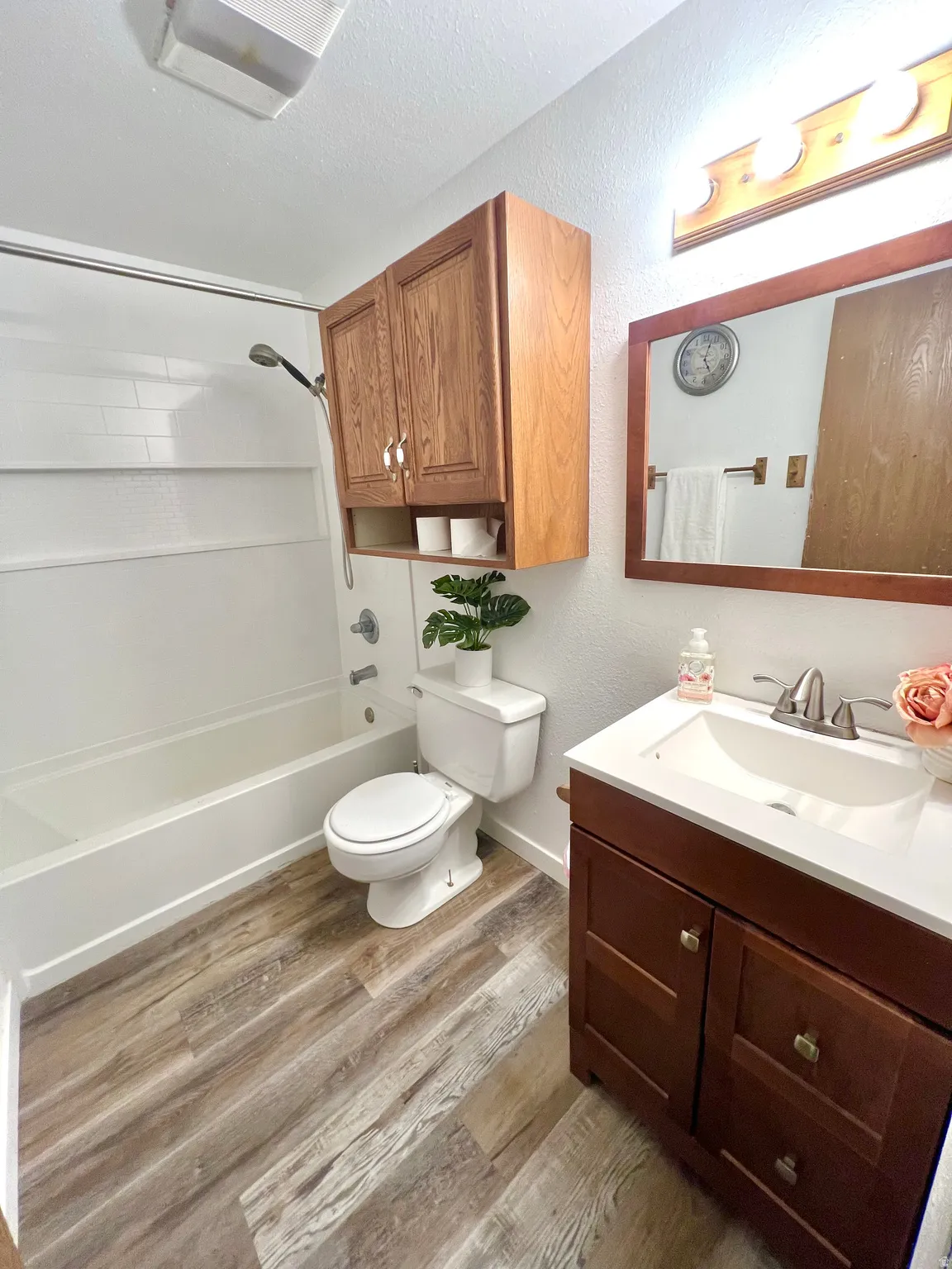 Bathroom featuring wood-finish flooring, a white tub with shower, and a toilet