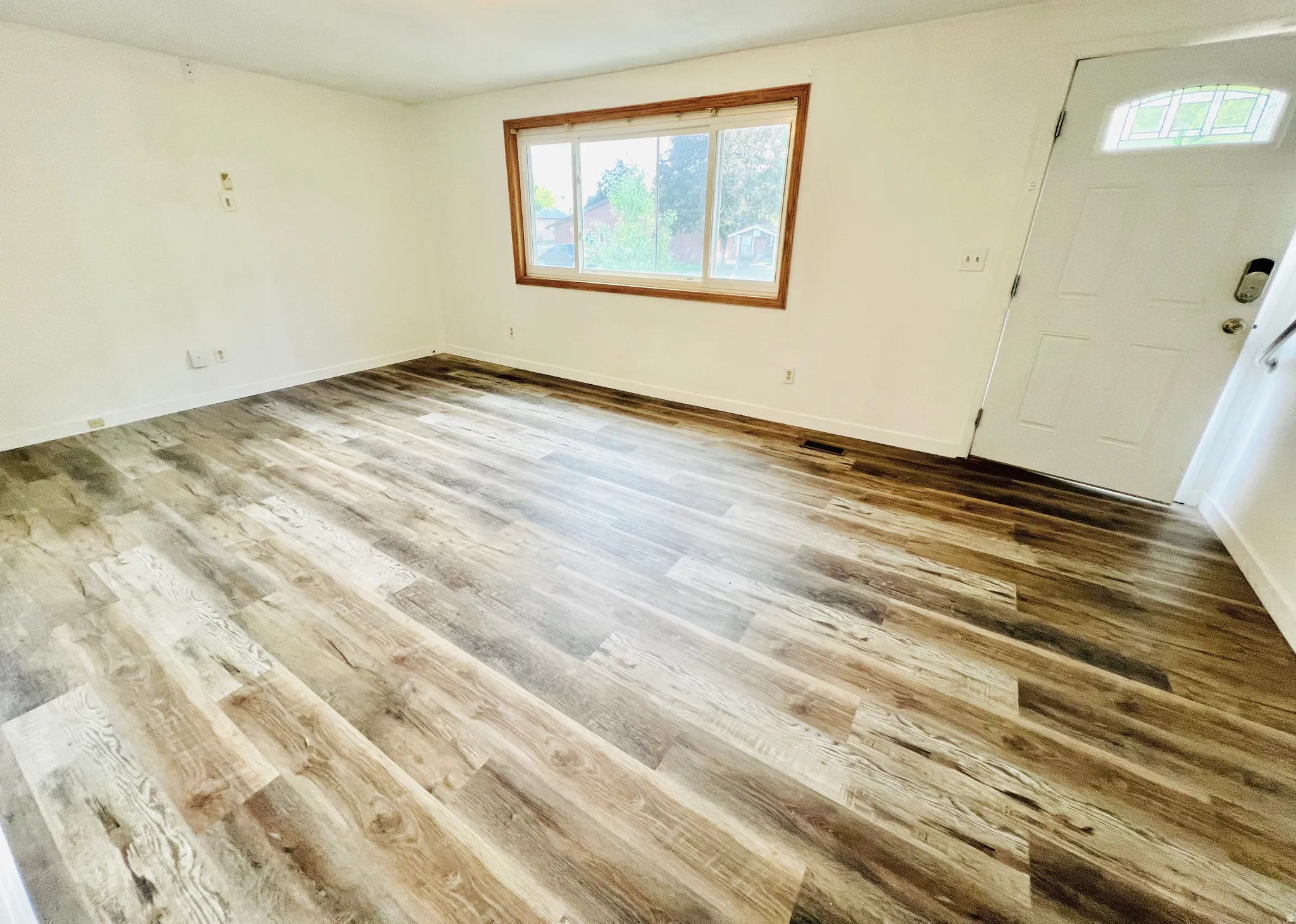 Expansive room featuring wood-finish flooring, a large window with wood trim, and a white entry door with an arched glass insert