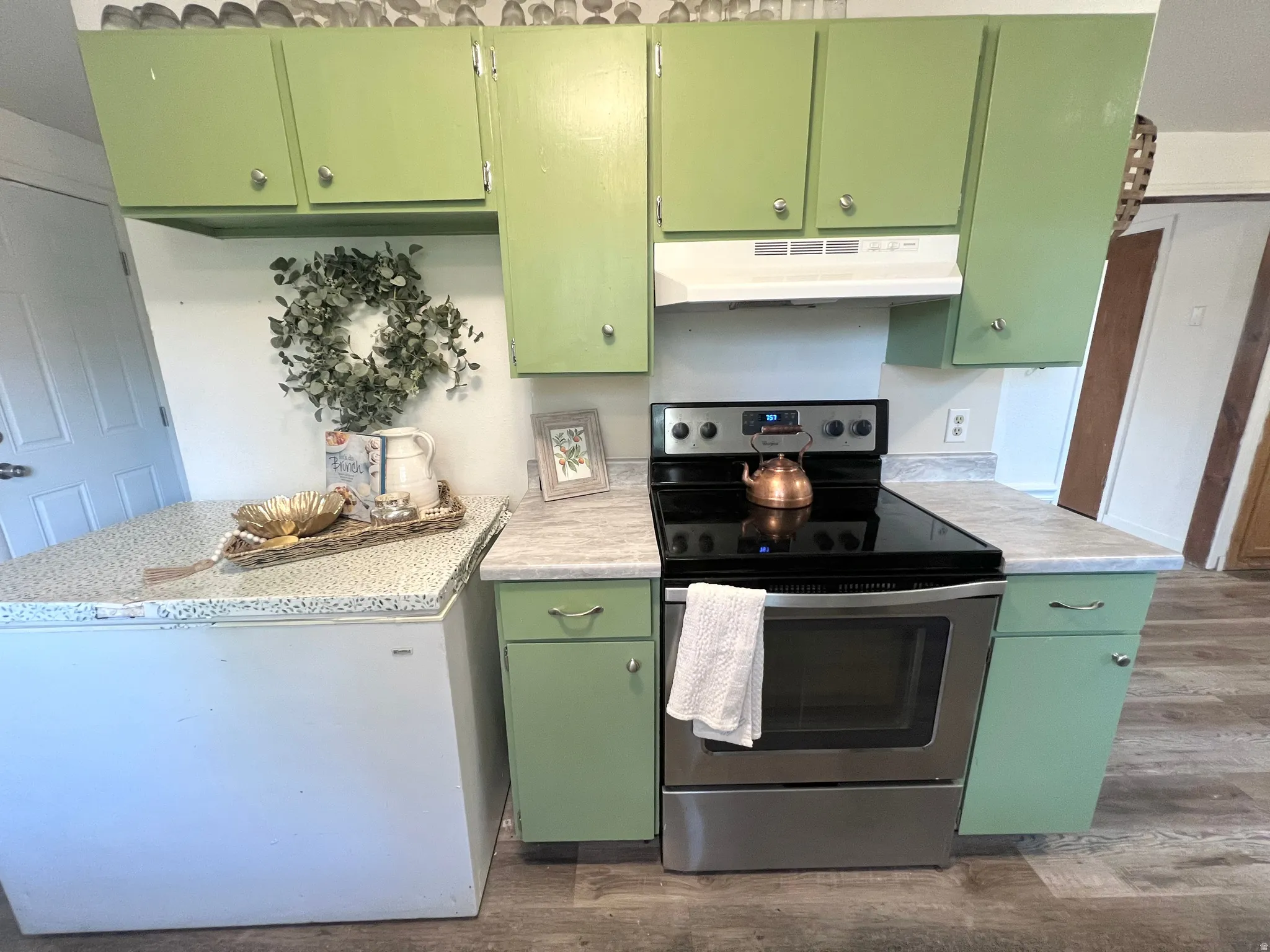 Kitchen featuring green cabinetry, light-toned countertops, and wood-finish flooring