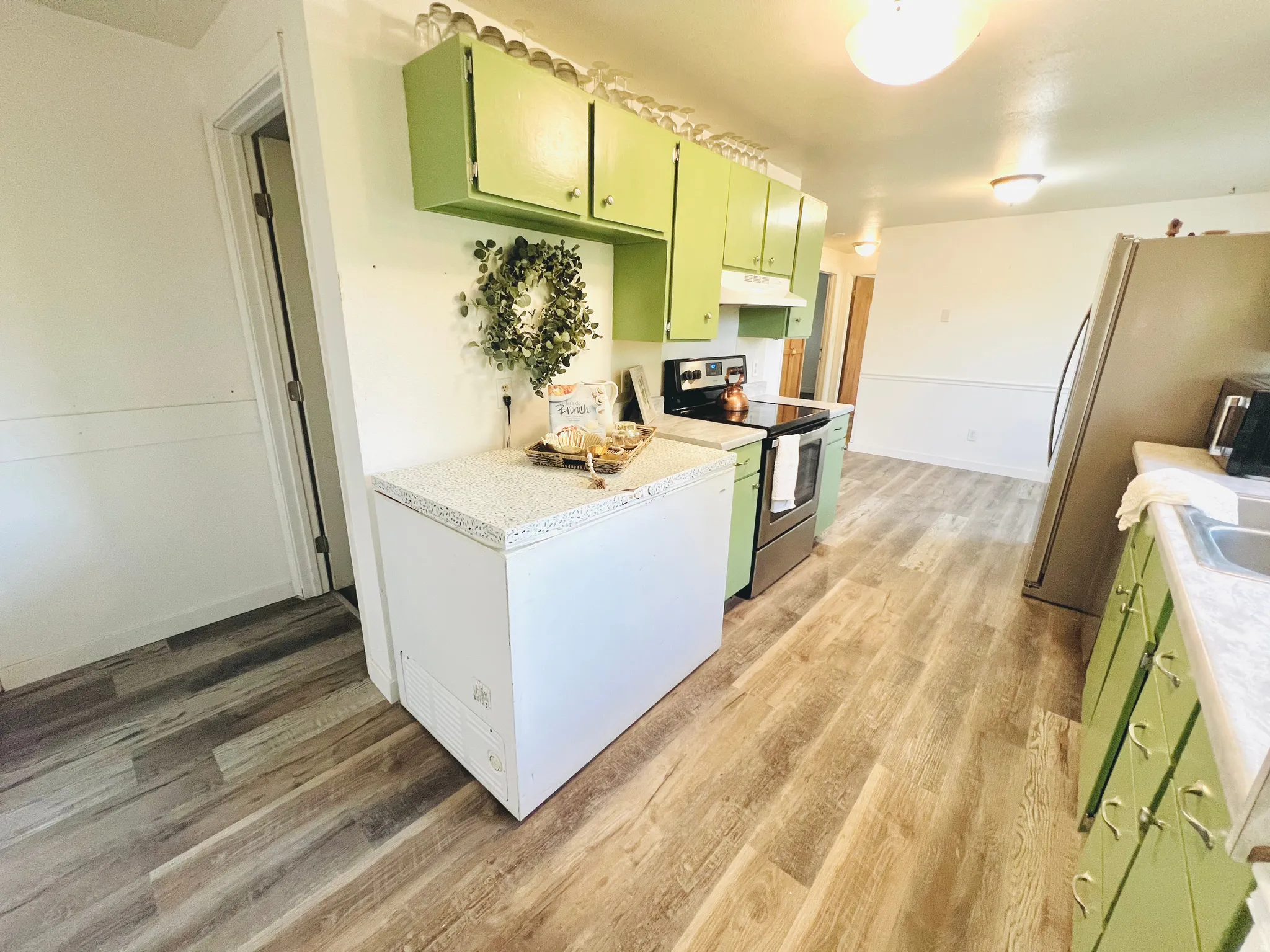 Kitchen featuring wood-finish flooring, green cabinetry, white countertops, and stainless steel appliances