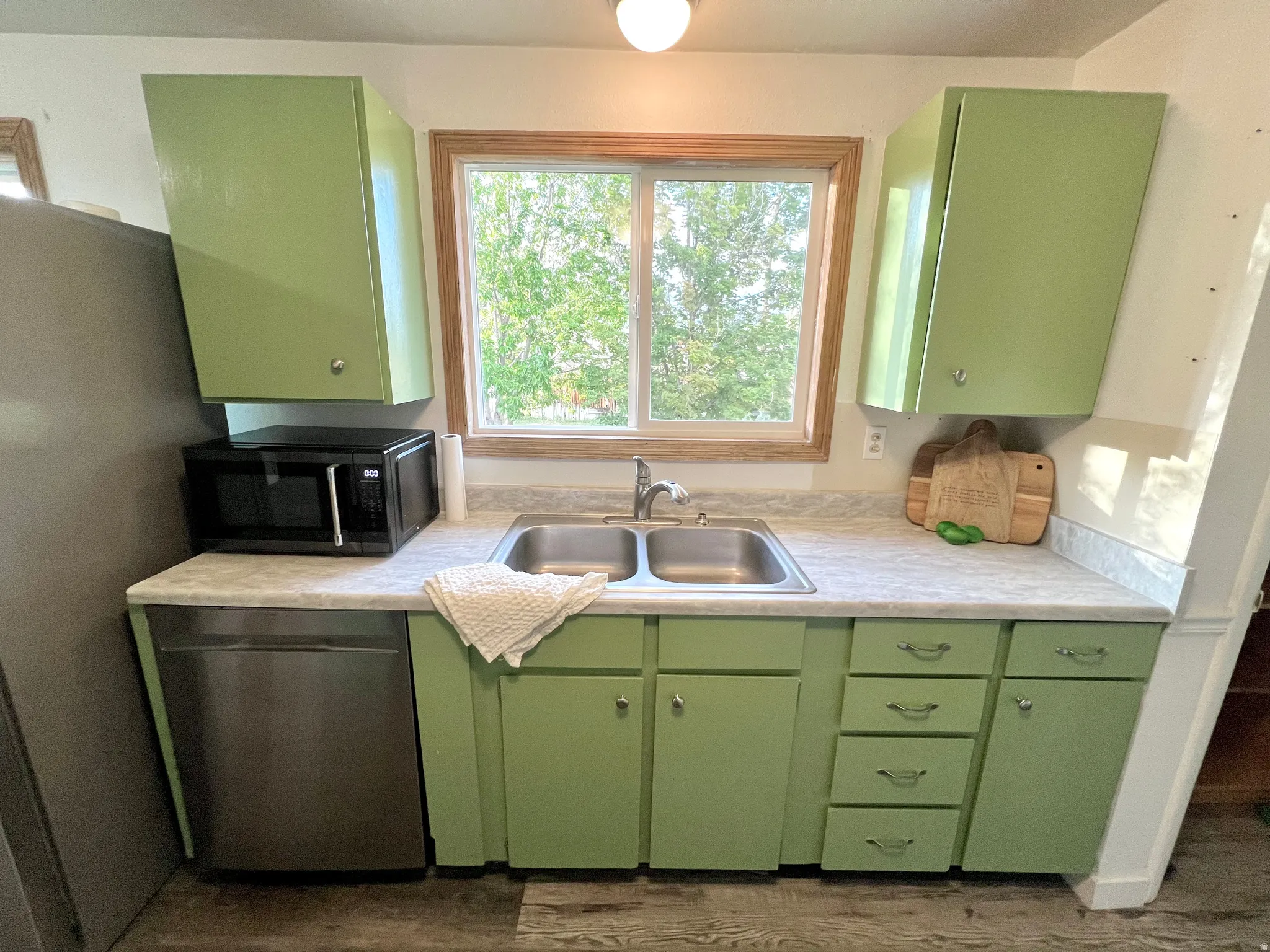 Kitchen featuring a double basin stainless steel sink with a window above, light green cabinetry, and wood-finish flooring
