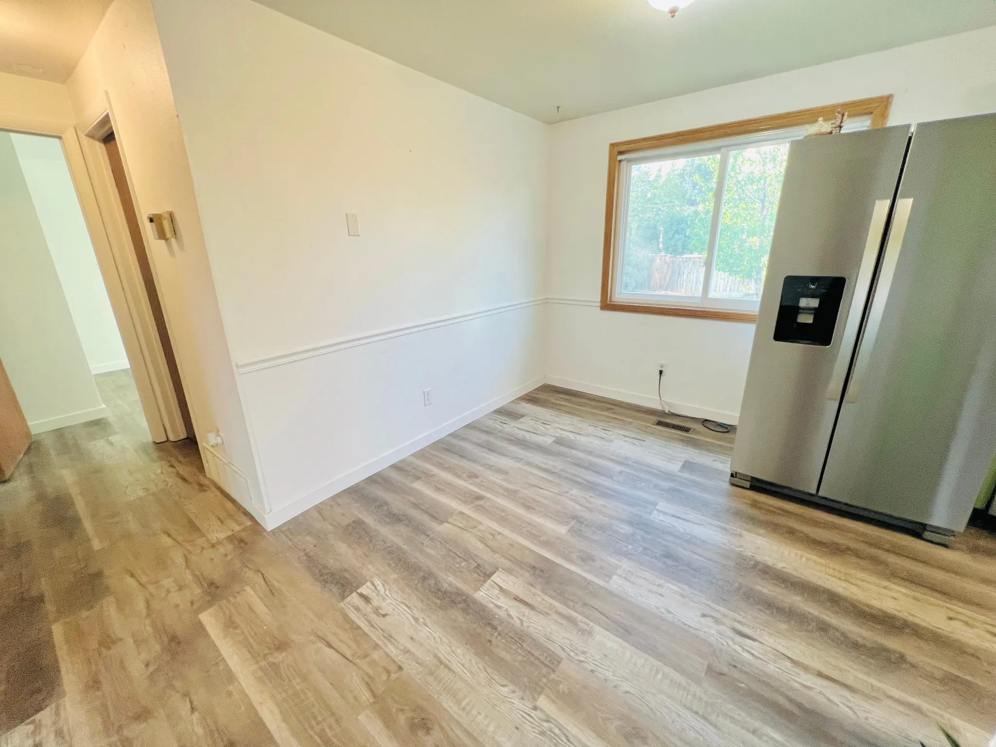 Spacious room featuring wood-finish flooring, white walls, and wainscoting detail