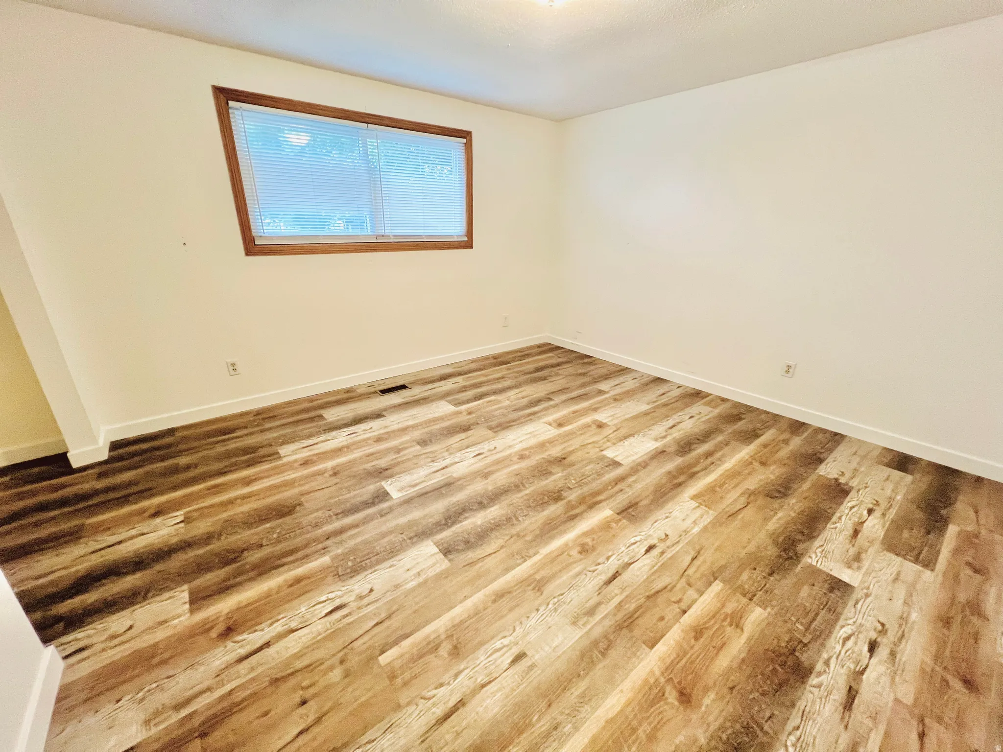 Spacious room featuring wood-finish flooring, white baseboards, and a window with wood trim