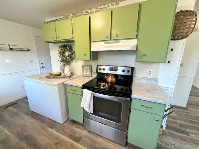 Kitchen featuring wood-finish flooring, light-toned countertops, green cabinetry, and a stainless steel range with overhead ventilation