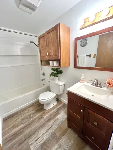 Bathroom featuring wood-finish flooring, a white tub with shower, and a toilet