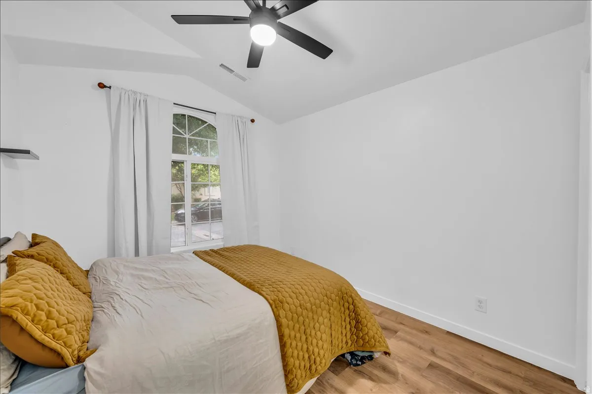 Vaulted ceilings featuring a modern ceiling fan, an arched window with white trim, wood-finish flooring, and a floating wall shelf