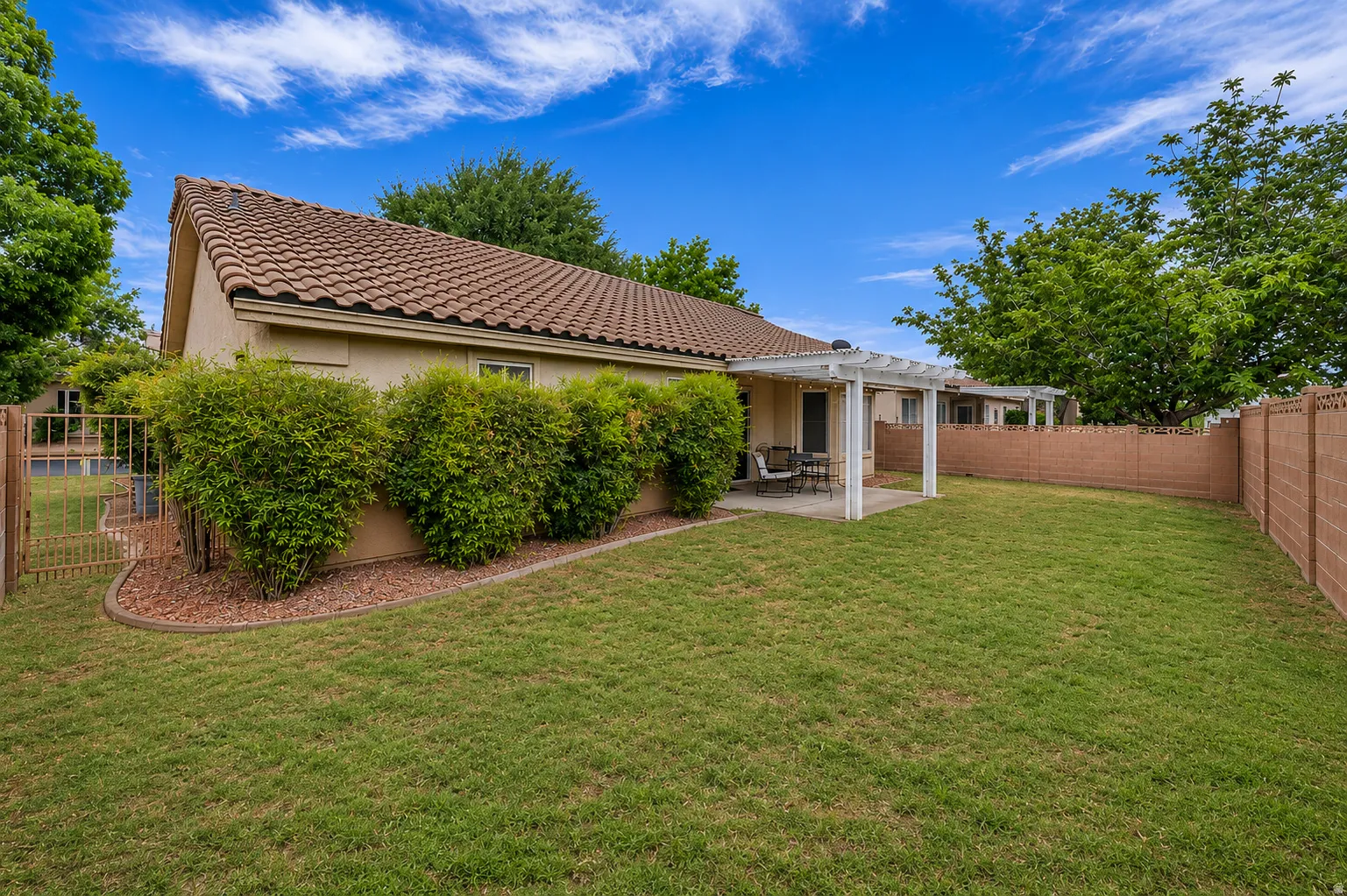 Expansive rear yard featuring a covered patio with a white pergola, a large grass lawn, and mature privacy shrubs