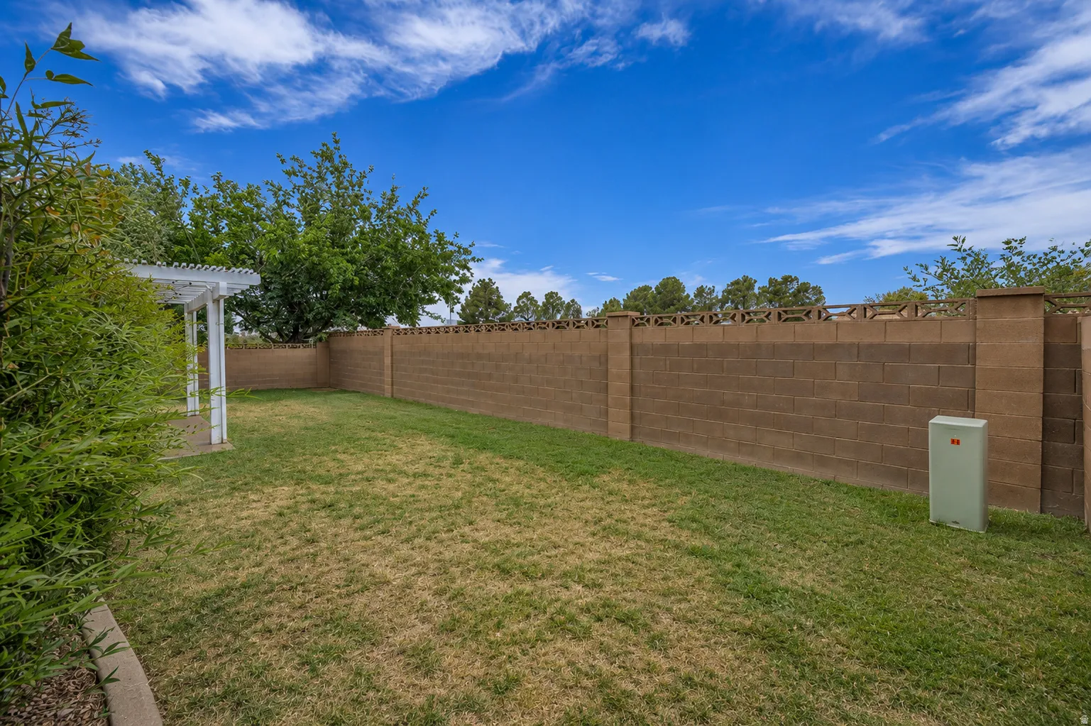 Expansive backyard featuring a manicured lawn, a solid block wall perimeter, and a white pergola structure