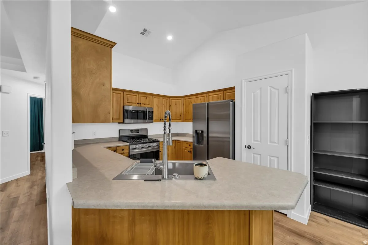 Kitchen featuring a large peninsula with an undermount sink, wood-finish cabinetry, stainless steel appliances, vaulted ceilings, and recessed lighting