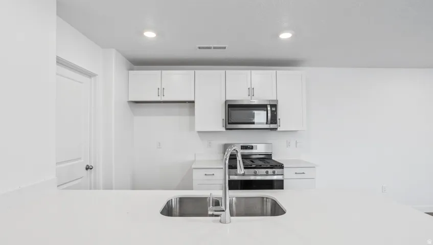 Kitchen featuring a stainless steel undermount sink, gooseneck faucet, white cabinetry with silver hardware, stainless steel microwave, and a gas range