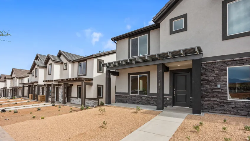 Contemporary townhome exterior featuring a dark entry door, stone facade accents, stucco siding, and a decorative pergola over the entry