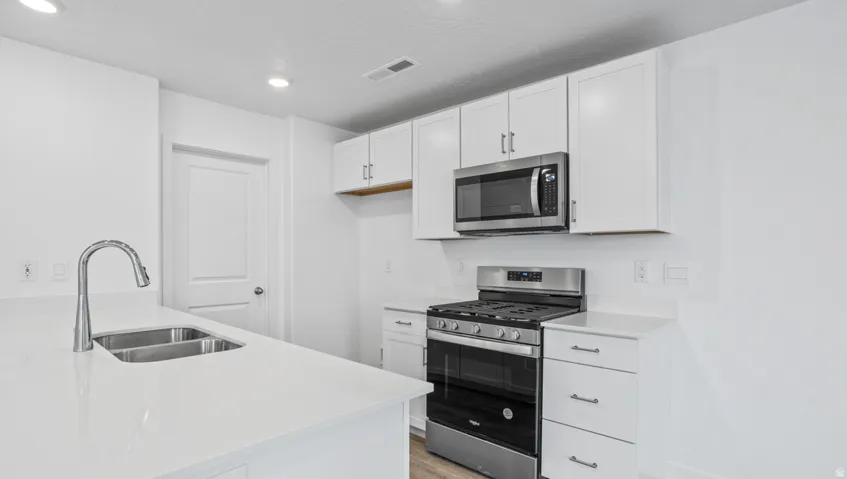 Modern kitchen featuring white cabinetry, stainless steel appliances, a gas range, and a dual basin sink with a gooseneck faucet