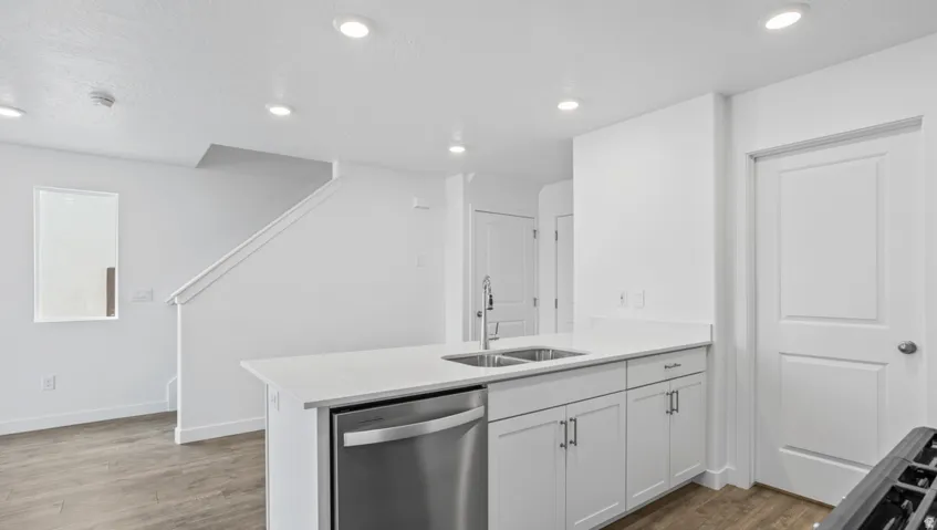 Modern kitchen island with a double basin stainless steel sink, white cabinetry, and a built-in stainless steel dishwasher