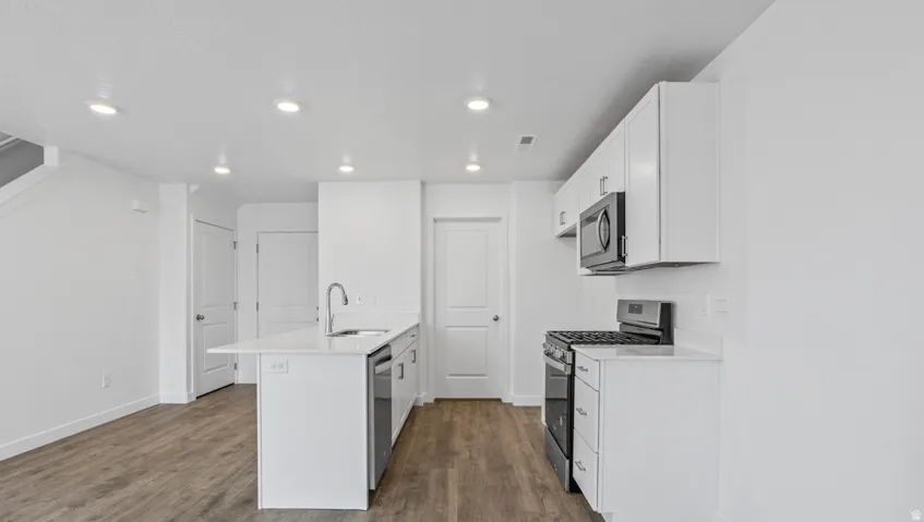 Kitchen featuring white cabinetry, stainless steel appliances, an island with an integrated sink, white countertops, and wood-finish flooring