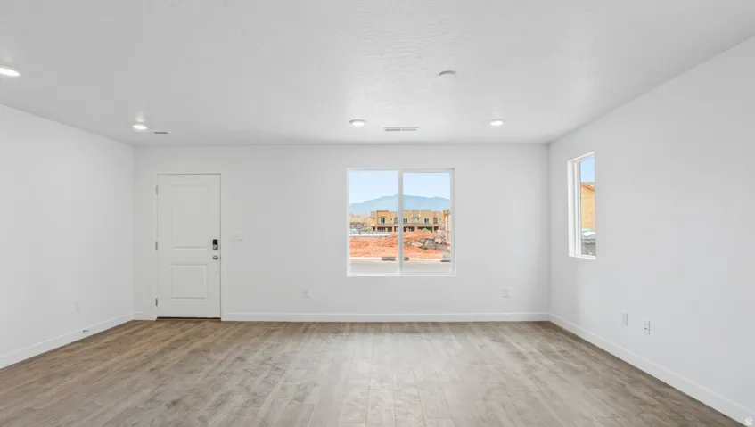 Spacious room featuring wood-finish flooring, white walls, and recessed lighting
