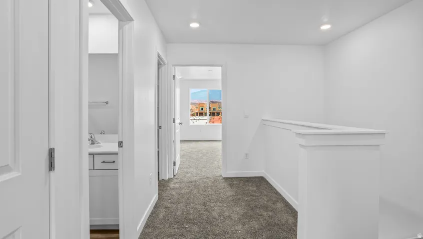 Carpeted hallway featuring white walls, recessed lighting, and a white balustrade