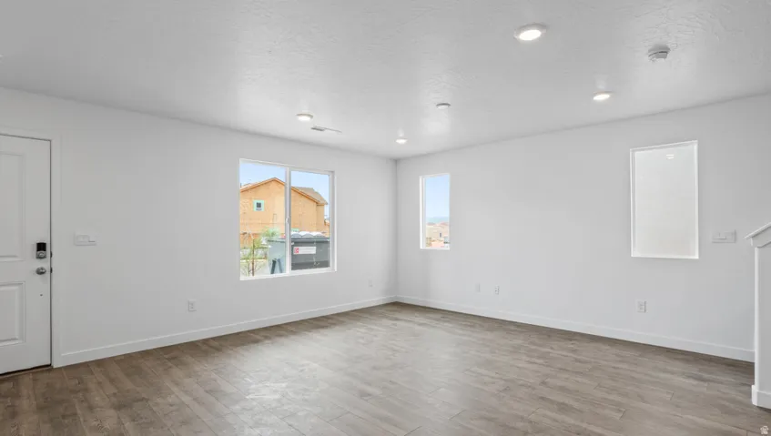 Open-concept room featuring wood-finish flooring, recessed lighting, multiple windows, and a white entry door with smart lock hardware