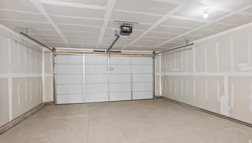 Spacious garage with unfinished walls, concrete flooring, overhead lighting, and an automatic garage door opener