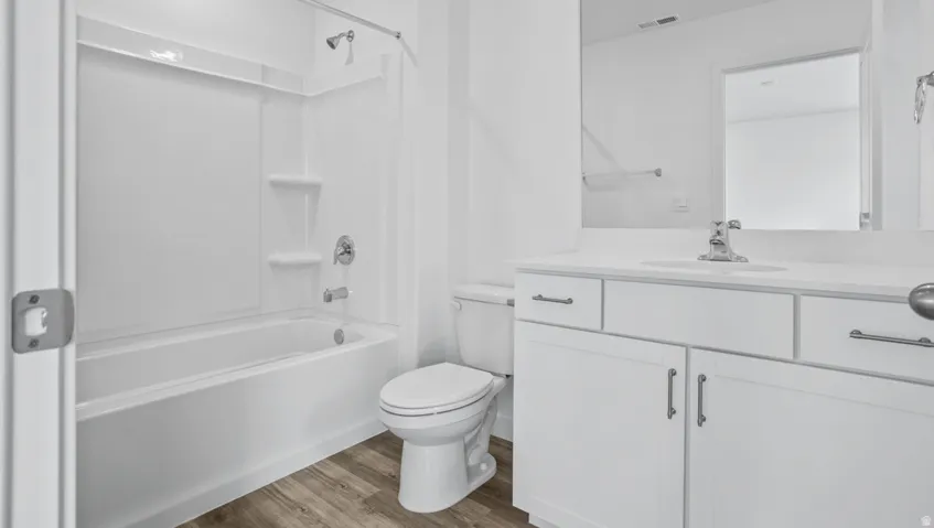 Bathroom featuring a white vanity with cabinet and drawer storage, an integrated sink, a large wall mirror, and a white toilet