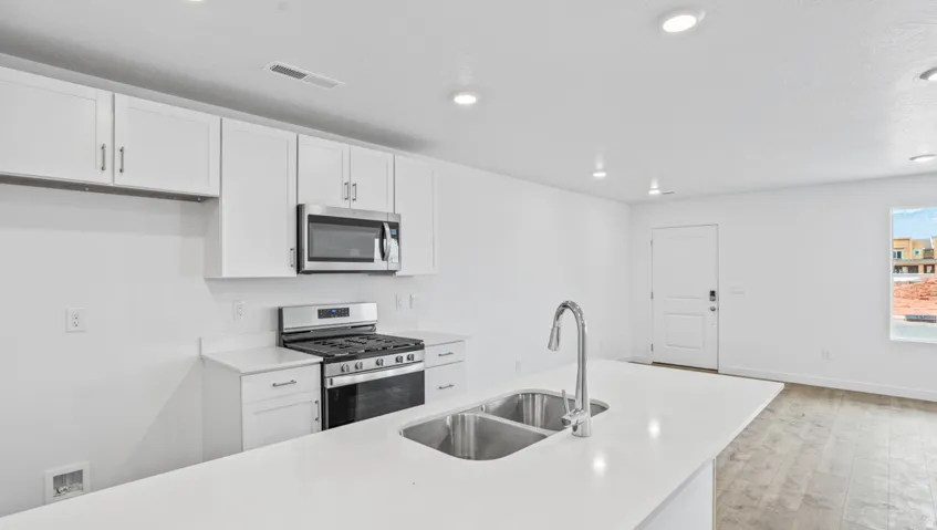 Contemporary kitchen featuring white cabinetry, stainless steel appliances, and a central island with a double basin sink