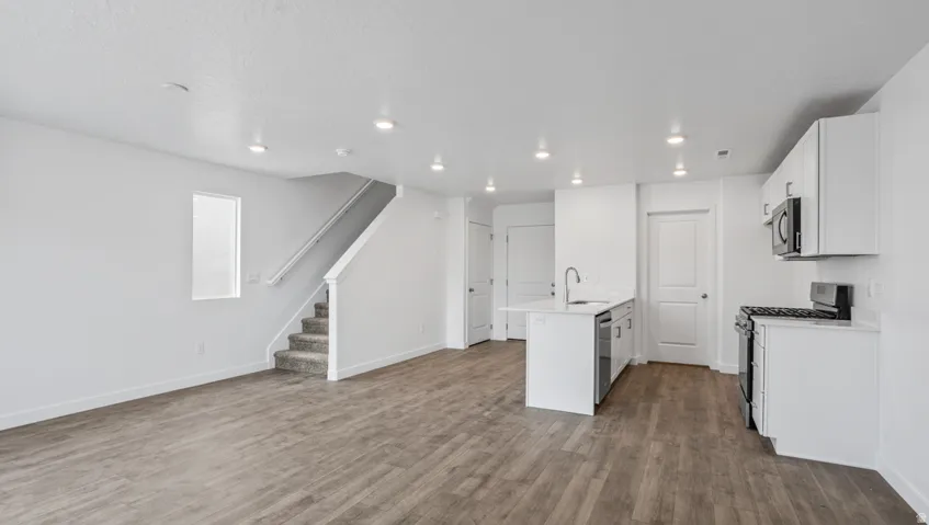 Open-concept living area featuring wood-finish flooring, recessed lighting, and a white kitchen with a peninsula island