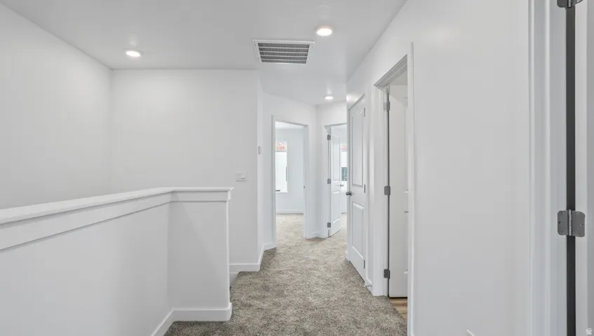 Hallway featuring recessed lighting, white walls, gray carpet, multiple white interior doors, and a white stair railing
