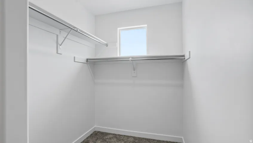 Walk-in closet featuring white wire shelving, hanging rods, an upper window, and carpet flooring