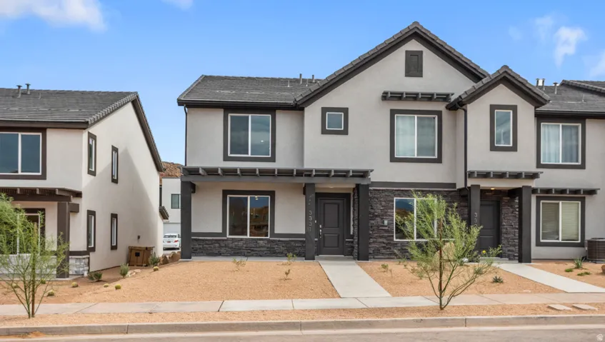 Contemporary townhome exterior featuring light stucco siding, dark trim, a dark shingle roof, and a stone facade accent