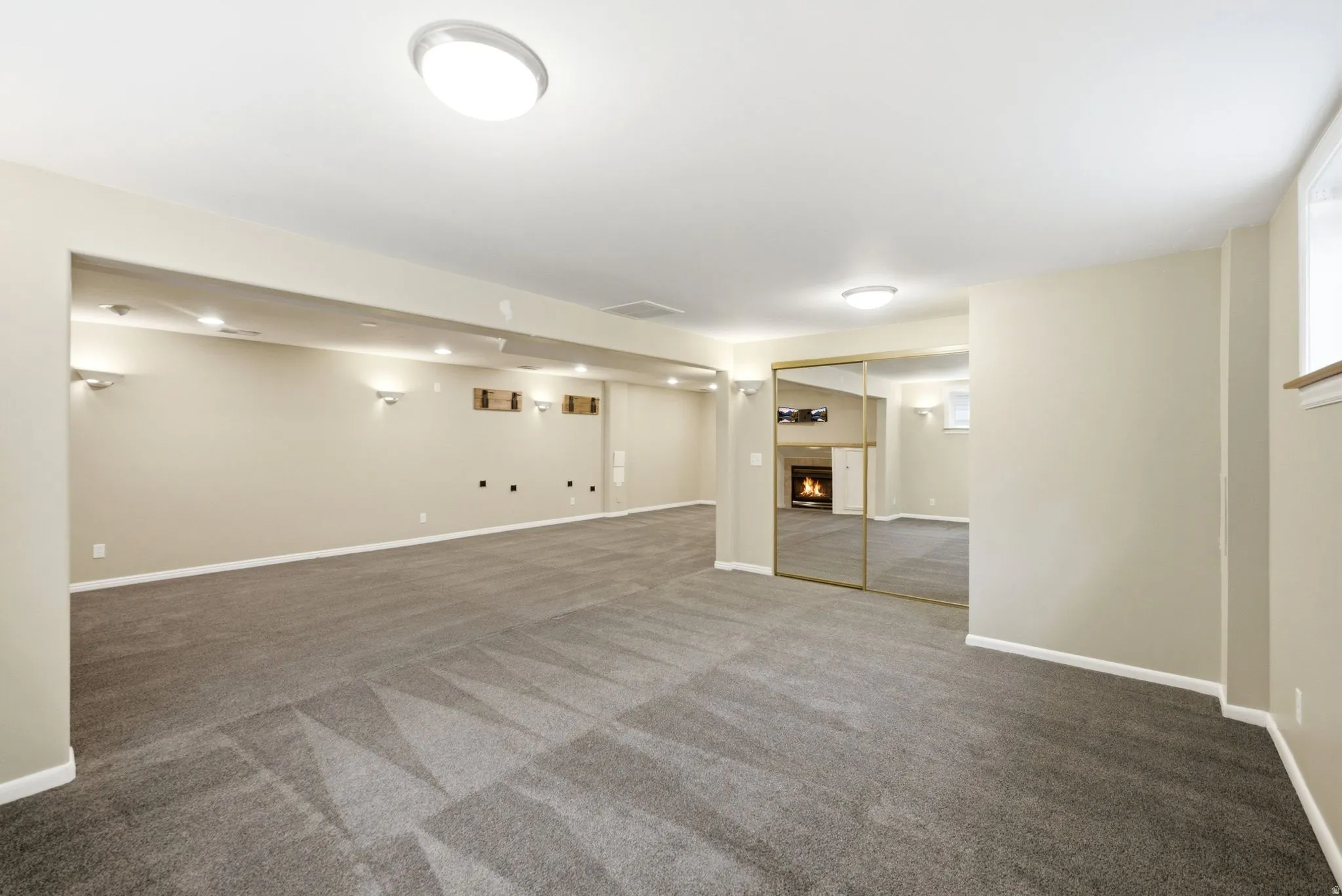 Spacious room featuring patterned gray carpeting, light-toned walls, recessed lighting, and wall sconces