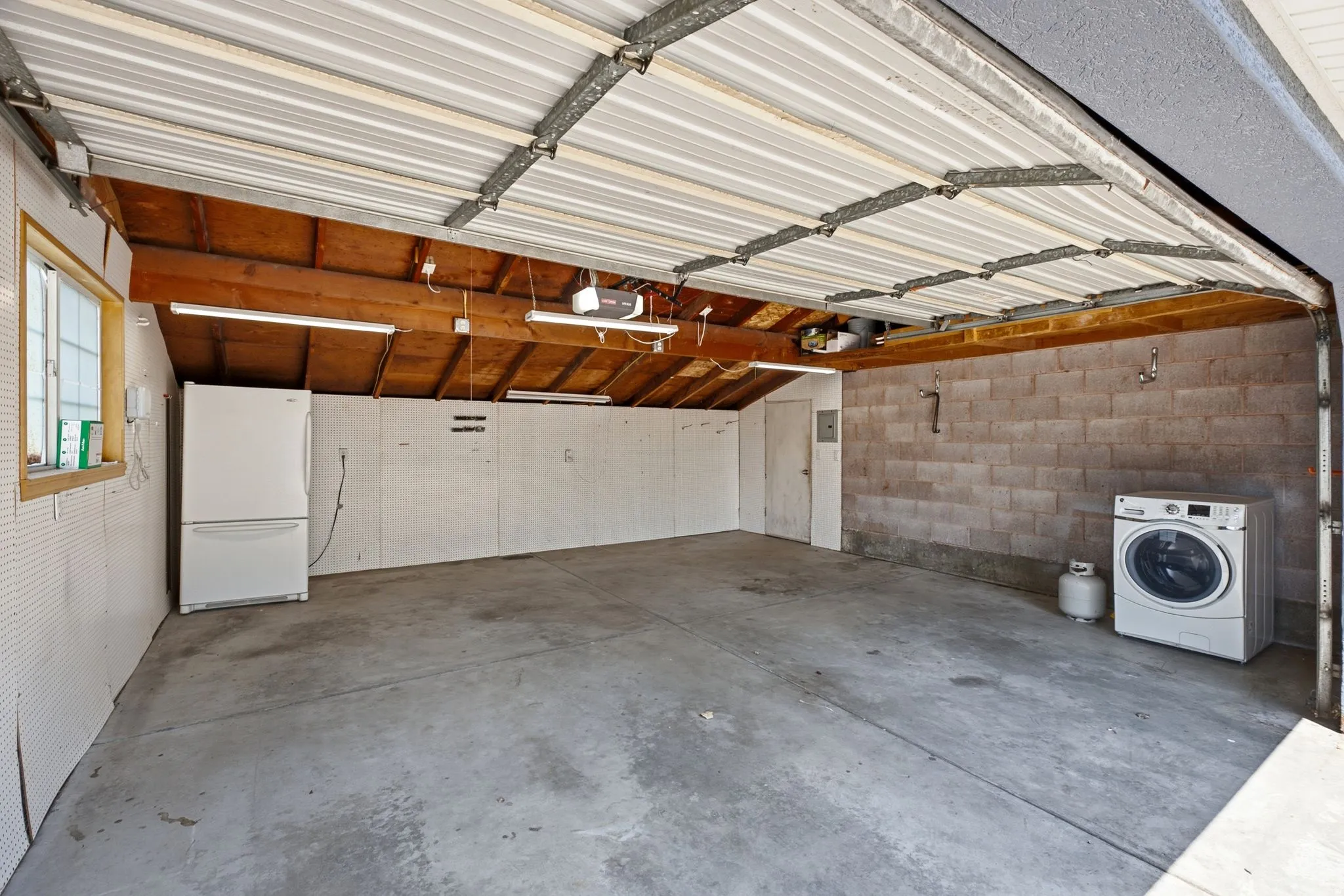 Spacious garage featuring a concrete floor, exposed wood beam ceiling, block wall construction, and a window for natural light