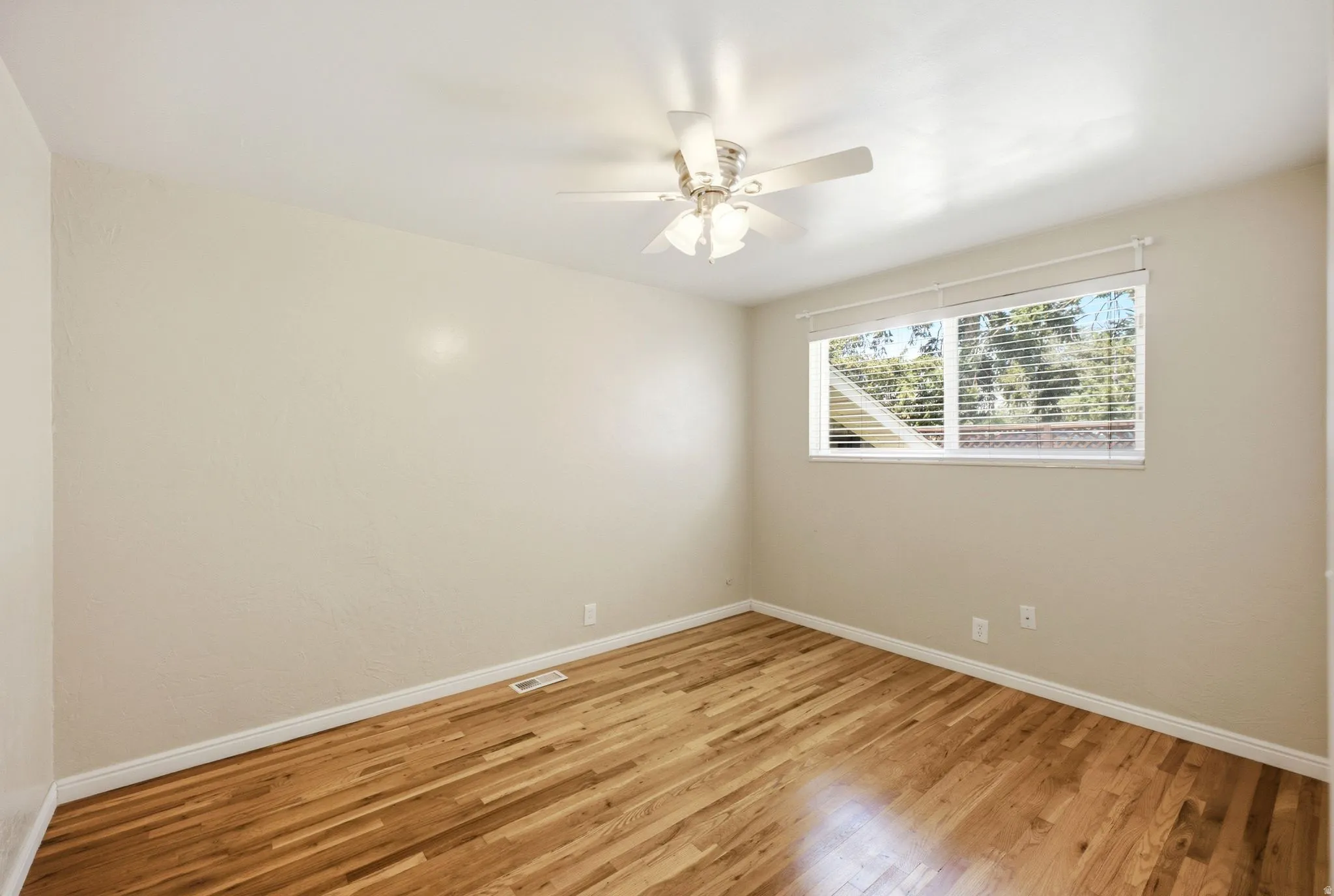 Room featuring wood-finish flooring, a ceiling fan with integrated lighting, and a window with horizontal blinds