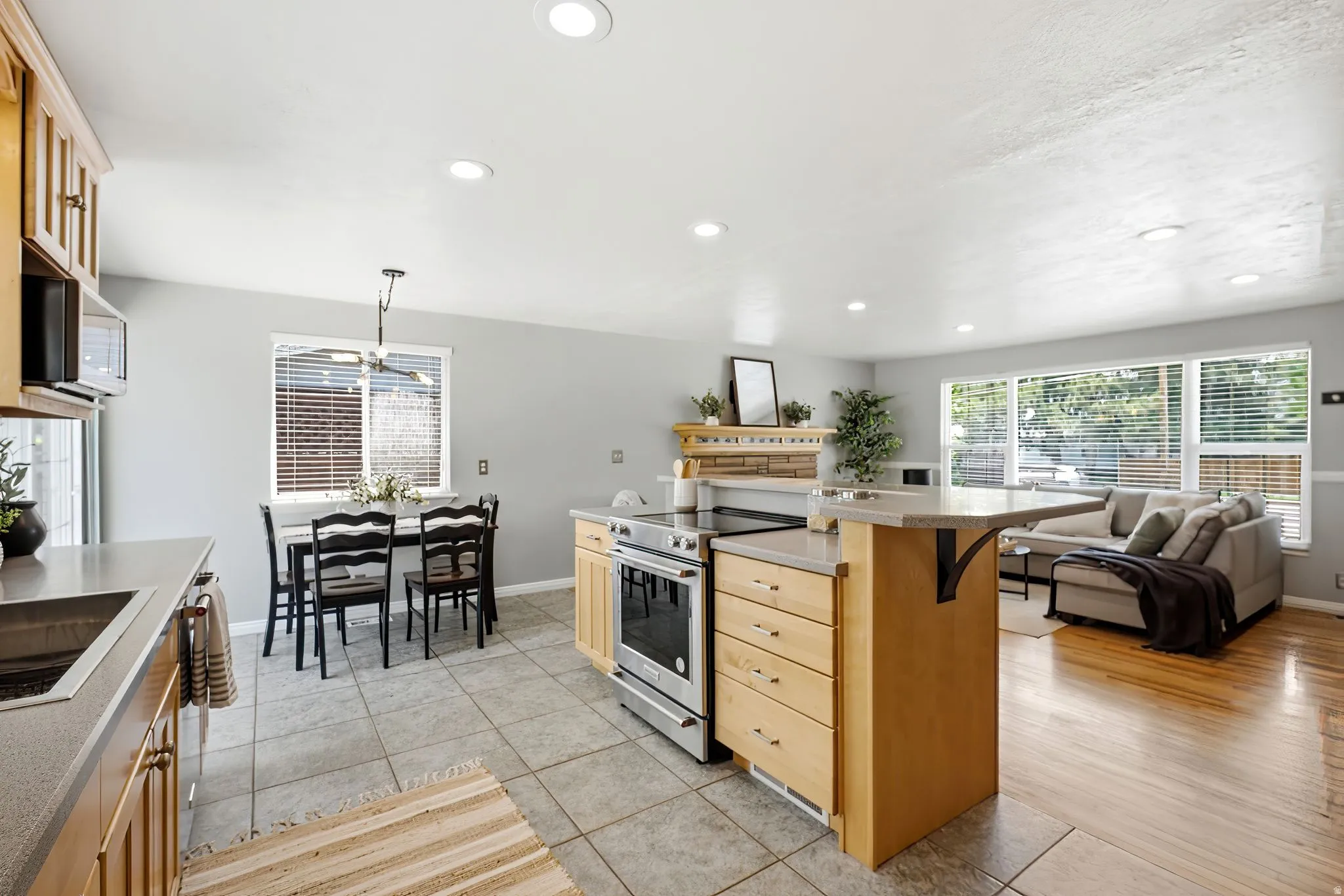 Open-concept living area featuring a kitchen island with built-in stainless steel range, light wood cabinetry, recessed lighting, and wood-finish flooring in the seating area
