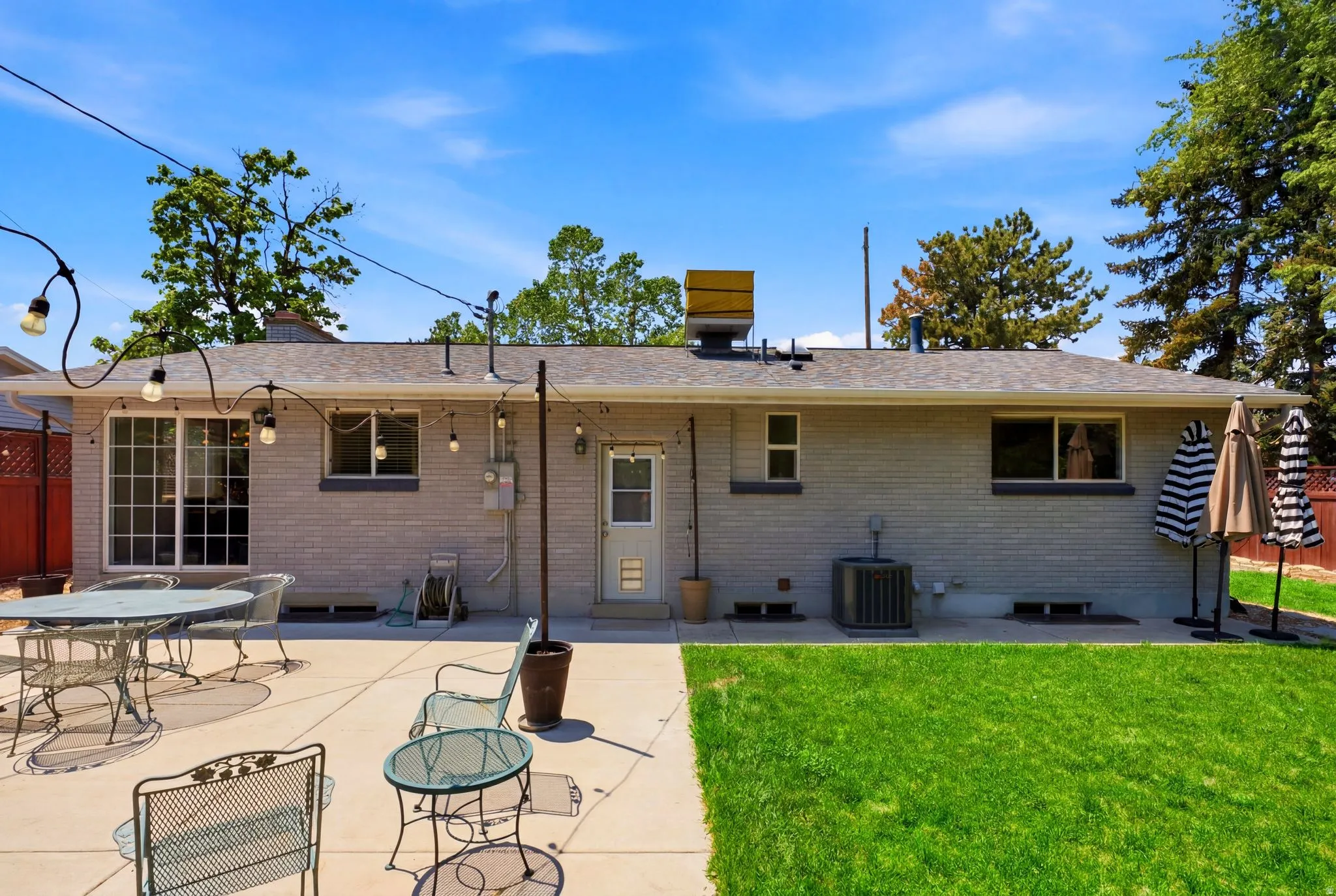 Expansive backyard featuring a concrete patio, verdant lawn, and a light-colored brick exterior