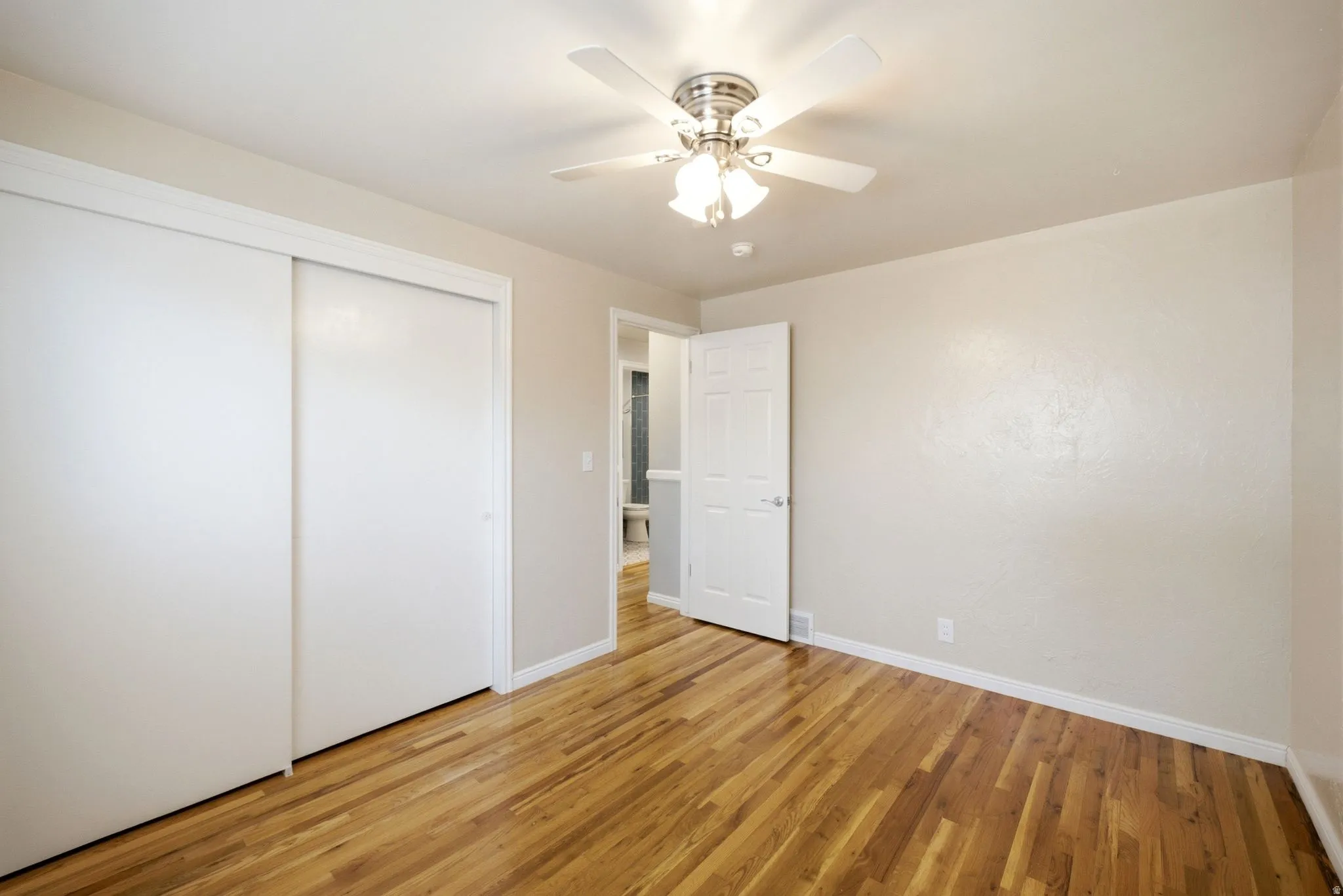 Bedroom featuring wood-finish flooring, a ceiling fan with integrated lighting, and a sliding door closet